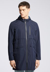 Granatowa wodoodporna kurtka z kapturem, z przednim zamkiem błyskawicznym, dwiema dużymi kieszeniami z przodu oraz kieszenią na zamek błyskawiczny na piersi do bezpiecznego przechowywania.