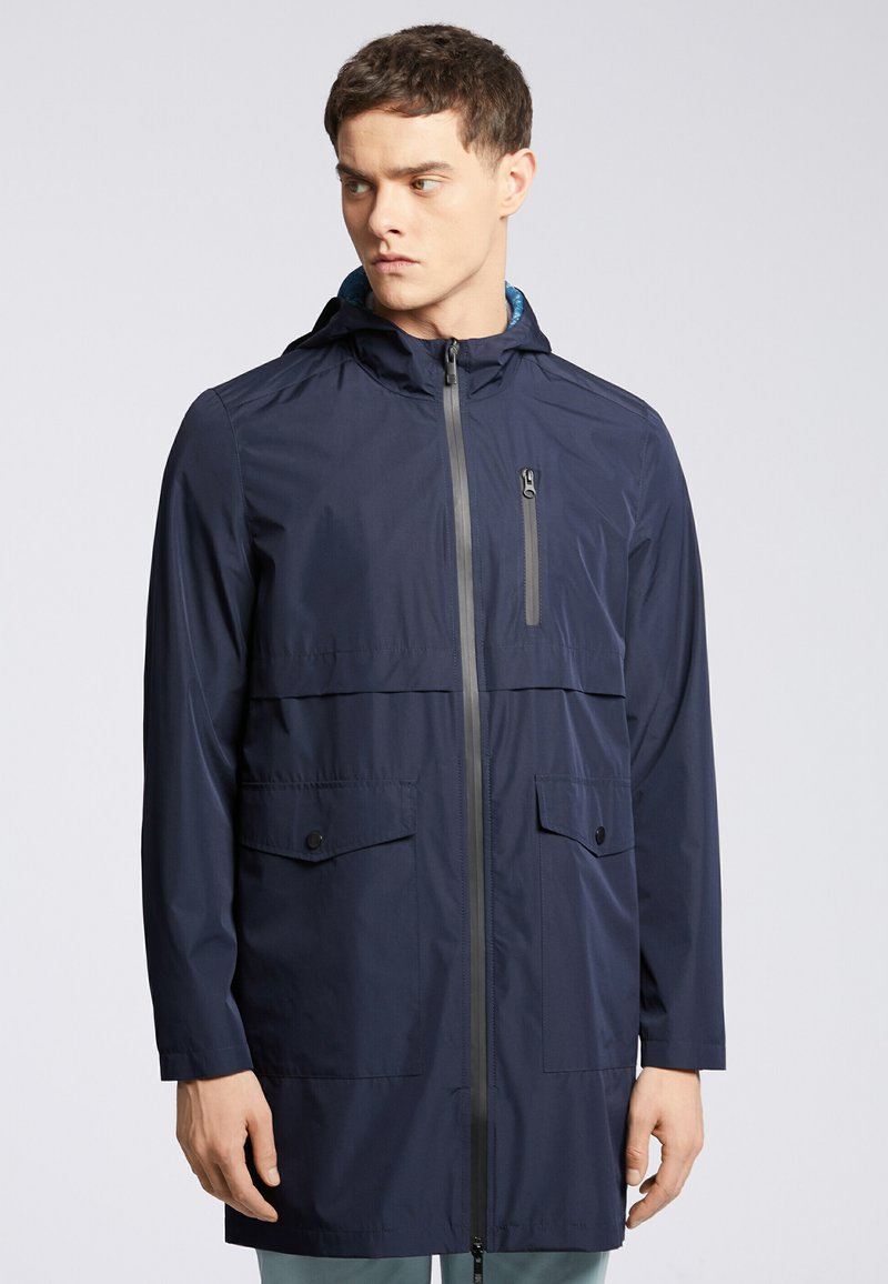 Granatowa wodoodporna kurtka z kapturem, z przednim zamkiem błyskawicznym, dwiema dużymi kieszeniami z przodu oraz kieszenią na zamek błyskawiczny na piersi do bezpiecznego przechowywania.