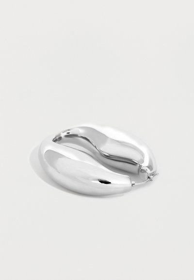 Χοντρά ασημένια σκουλαρίκια κρίκοι με λεία, στρογγυλεμένα επιφάνειες και γυαλιστερό, ανακλαστικό φινίρισμα, που βρίσκονται επίπεδα σε λευκό φόντο.