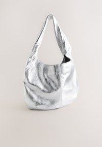 Ezüst fémes hobo táska texturált bőrből. Puha, laza forma, széles pánttal és nyitott topsal, amely sima belsőt mutat.