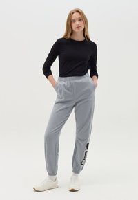 Graue Sweatpants mit elastischen Bündchen und einem Bund, versehen mit schwarzem "NYC" Schriftzug. Kombiniert mit einem taillierten langen schwarzen Oberteil und weißen Sneakers.