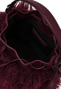 Burgunderfarbene Handtasche mit strukturiertem, plüschigem Äußeren, glattem Lederbesatz und einem dunklen Stoffinnenfutter mit Markenetikett.