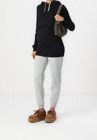 Svart huvtröja med snörning, grå sweatshirtbyxor och bruna plattformsskor. Huvtröjan har en kort design med en avslappnad passform.