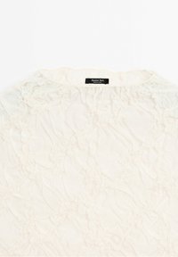 Blouse blanche texturée avec des détails de tissu froncé et une étiquette Massimo Dutti au niveau de la nuque.