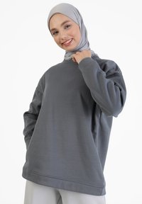 Sudadera gris con cuello redondo, mangas largas y un ajuste relajado. Presenta una textura suave y detalles de costura mínimos.