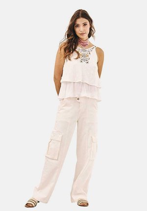 Top blanco de capas con diseño recortado de flores, combinado con pantalones cargo beige claro que cuentan con múltiples bolsillos y piernas anchas.