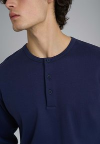 Maglietta Henley a maniche lunghe di colore blu navy realizzata in tessuto morbido, con scollatura rotonda, pattino con tre bottoni e dettagli di cucitura minimi.
