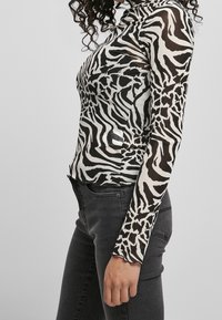 Svart och vit långärmad topp med zebra-printmönster, tillverkad av ett transparent tyg, figurnära design, kombinerad med mörka jeans.