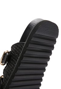 Sandale en toile noire avec une sangle texturée, dotée d'une boucle en or et d'une semelle en caoutchouc nervurée pour l'adhérence et la durabilité.