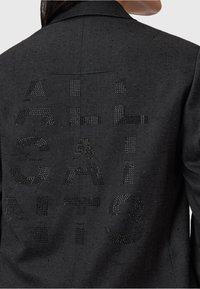 Blazer nero con un tessuto strutturato. Presenta una grande scritta in contrasto sul retro, realizzata con strass lucidi. Design strutturato.