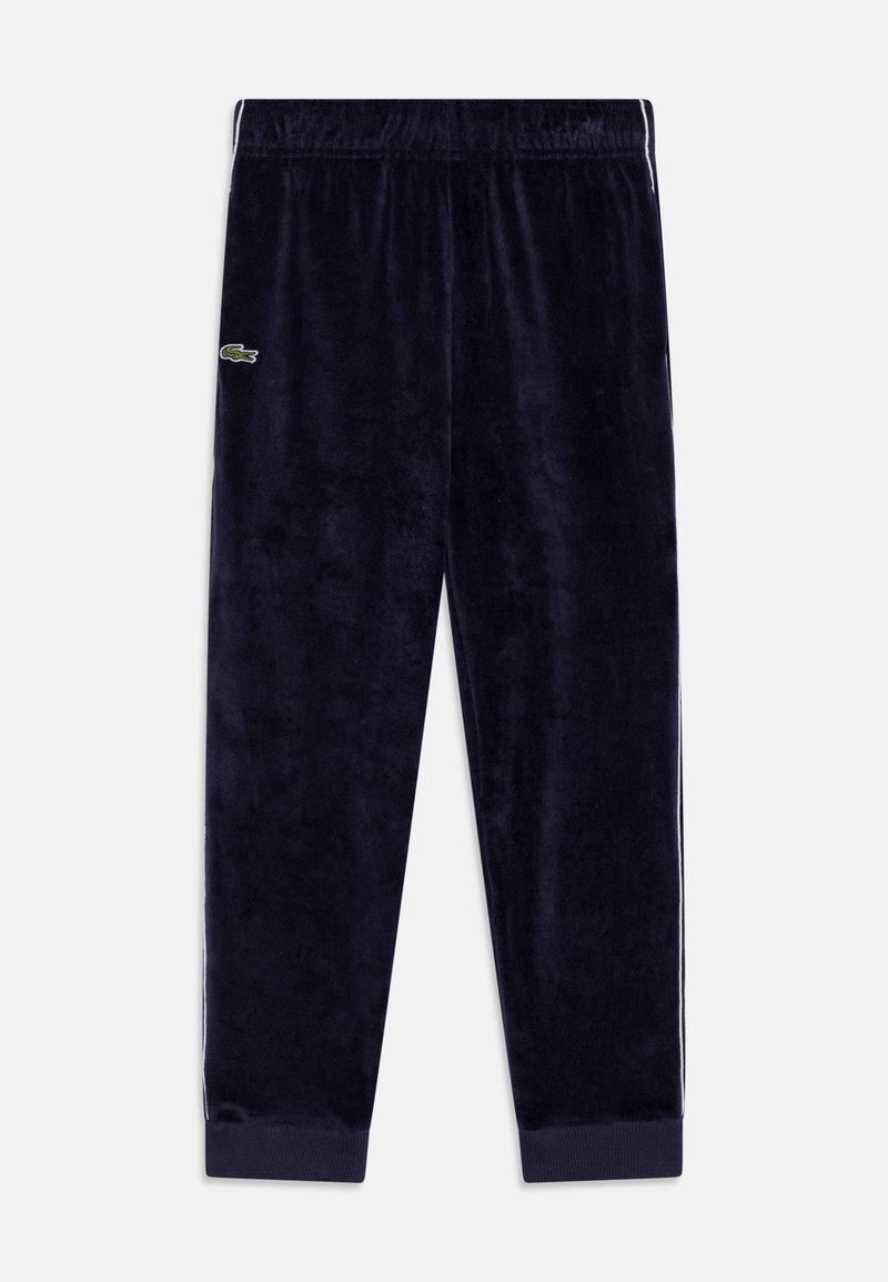 Pantaloni da tuta in velluto blu navy con elastico in vita, polsini a costine, strisce laterali e piccolo logo di coccodrillo verde sulla coscia sinistra.