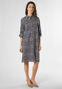 Shiffonkleid mit navyblauem und cremefarbenem Muster, mit Kragen, hochgekrempelten Ärmeln und lockerer Passform bis zur Mitte der Wade. Mit Knöpfen geschlossen.