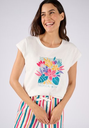 T-shirt en coton blanc présentant un imprimé floral aux couleurs vives avec le texte "Nuit Tropicale", associé à un pantalon rayé multicolore.
