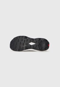 Semelle de chaussure en caoutchouc noir avec un motif de traction texturé, dotée d'un bord blanc et d'un accent rouge. Le design garantit une adhérence et une durabilité.