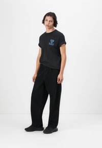 Black cotton t-shirt with blue printed text "RIDE THE RAILS," paired with loose-fitting black jeans and black sneakers.