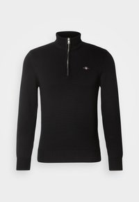 Pull noir en maille côtelée avec manches longues, demi-fermeture éclair au col montant et petit logo brodé sur le côté gauche de la poitrine.