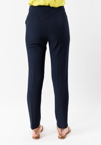 Pantaloni blu navy realizzati in tessuto liscio, con una vestibilità su misura, tasche laterali e cintura. Indossati con sandali color cuoio.