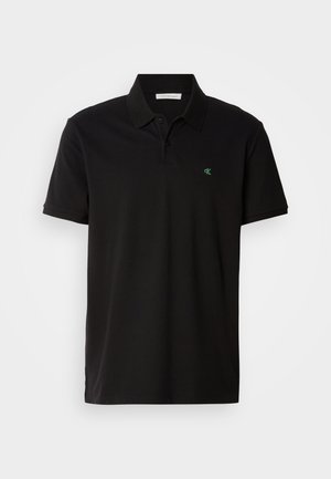 Polo shirt nera in cotone, con colletto classico, maniche corte e un piccolo logo verde sul lato sinistro. I bordi sono rifiniti in modo ordinato.