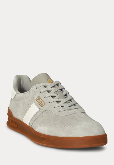 Šviesiai pilkas verstos odos sportinis batelis su balta juostele, ruda guminė pada, pilkosiomis raištelėmis ir „Polo“ logotipu šone ir liežuvėlyje.