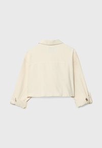 Zkrácená béžová bunda s límcem, dlouhými rukávy ohrnutými na manžetách a se švem přes zadní část pro zvýraznění detailu. Jemná textura.