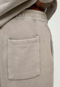 Beige sweatpants met een gestructureerde stof, een elastische tailleband en een opvallende zijzak. Minimalistisch ontwerp met zichtbare stiksels.