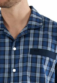 Kurzarmhemd mit blau-weißem Karomuster aus leichtem Stoff. Verfügt über eine Tasche mit einem dunkelblauen Akzent und weißen Knöpfen.