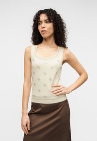 Μπεζ αμάνικη μπλούζα με υφή και τετράγωνο ντεκολτέ. Φορεμένη με καφέ σατέν φούστα που αναδεικνύει το στενό της σχέδιο.