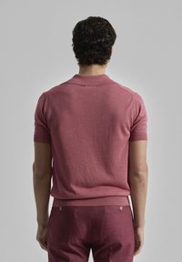 Camisa polo de manga corta y ajustada en tejido de punto color rosa claro con cuello plano y bordes acanalados, combinada con pantalones sastre a juego.
