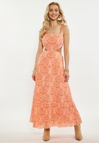 Rochie maxi portocalie cu detalii decupate. Prezintă un model ondulat și bretele. Este completată de cizme scurte bej deschis.