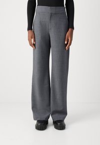 Pantalons gris à jambes larges en tissu texturé, dotés d'une taille lisse et associés à de grosses chaussures à plateforme noires.