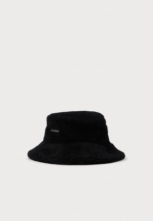 Zwarte fuzzy emmerhoed met een zachte textuur en een klein rechthoekig metalen logo-label aan de zijkant, tegen een witte achtergrond.