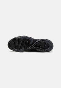 Black athletic shoe sole with a wavy, textured pattern and cut-out sections for enhanced grip. Rubber material provides flexibility and durability.