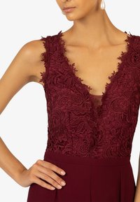 Bordeaux Spitzenkleid mit floralem Stickereien und tiefem V-Ausschnitt, kombiniert mit einem einfarbigen bordeauxfarbenen Rock und minimalen Hardware-Akzenten.