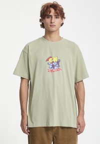 Lys grøn oversized t-shirt lavet af bomuld, med en farverig tegneserie grafik på forsiden. Korte ærmer og ribbet rund halsudskæring.