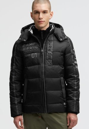 Black padded jacket with a hood, featuring stitched text, zip closure, side pockets, and grey accents on sleeves. Textured and quilted design.