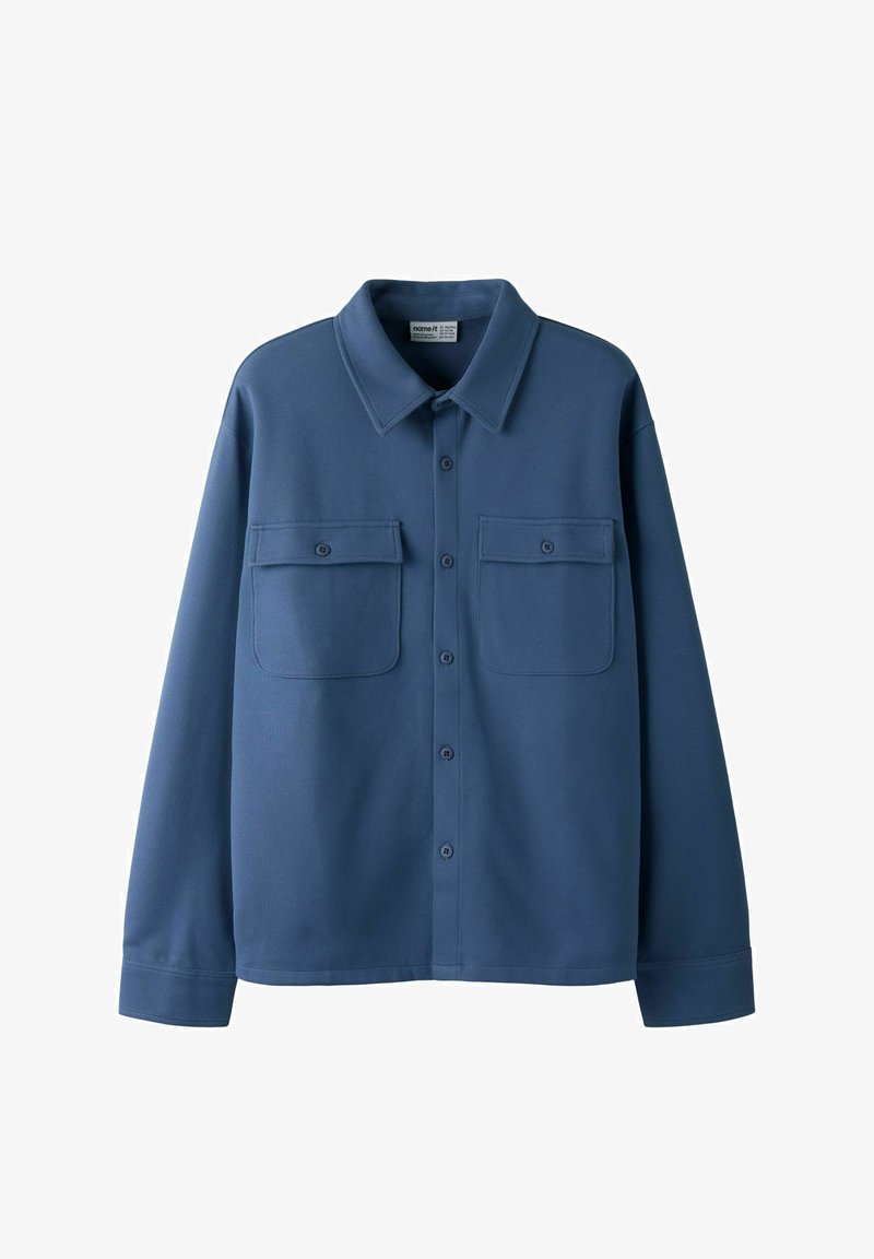 Chemise bleue à manches longues avec boutons, deux poches poitrine à l'avant et un col pointu, présentée sur un fond blanc.