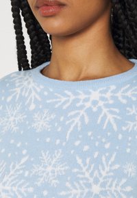 Hellblauer Pullover aus weichem Strickstoff mit weißen Schneeflockenmuster über die Oberfläche verteilt, mit einem Rundhalsausschnitt und gerippten Säumen.