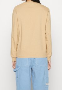 Långärmad skjorta i ljusbeige bomull med rund halsringning, med en avslappnad passform och ribbade muddarna, kombinerad med ljusblå cargo-byxor.