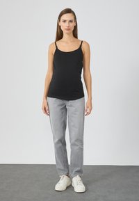 Μαύρο τοπ καμισόλ με λεπτές τιράντες, σε συνδυασμό με ανοιχτό γκρι παντελόνι ίσιας γραμμής και λευκά αθλητικά παπούτσια σε απλό φόντο.