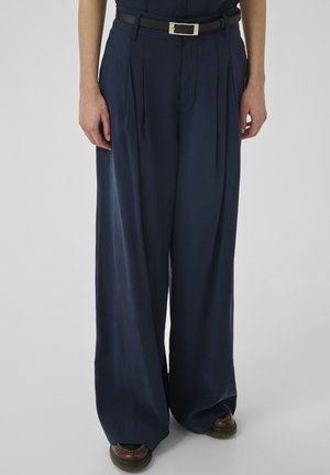 Granatowe spodnie plisowane o szerokich nogawkach, wykonane z gładkiego materiału. Posiadają czarny pasek z metalową klamrą.