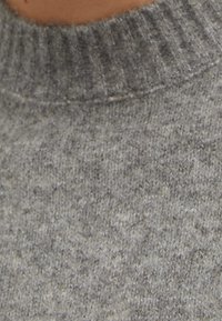 Pull gris en maille avec un col côtelé et une finition douce et texturée. Le tissu présente un motif chiné subtil sur toute sa surface.