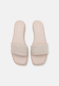 Béžové skluzavkové sandály s širokým látkovým páskem s raženým nápisem "Calvin Klein", měkkou stélkou a plochou podrážkou, s úhledně prošitým okrajem.