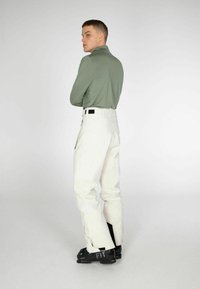 Witte sneeuwbroeken met een relaxed fit, gecombineerd met een groen shirt met lange mouwen. Zwarte skibotten maken de outfit compleet. Eenvoudig ontwerp, geen patronen.