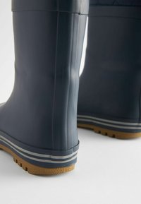 Bottes de pluie en caoutchouc navy avec un surface texturée et des semelles en caoutchouc beige. Caractéristiques : deux rayures horizontales grises près de la base.
