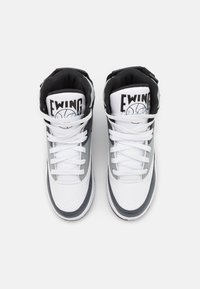 Paire de baskets montantes blanches, grises et noires avec des lacets blancs et le logo "EWING" sur la languette, vues de dessus sur un fond blanc.