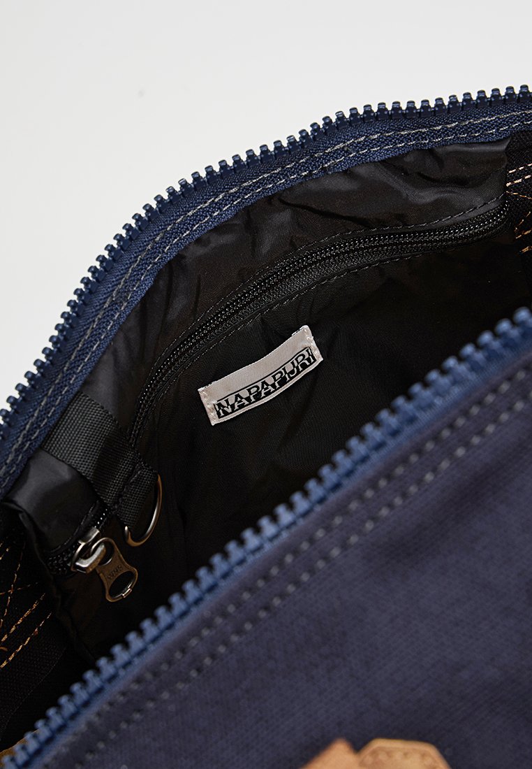Otwarta granatowa torba, w której widać czarną kieszeń na zamek błyskawiczny oraz metkę z nazwą marki "Napapijri."