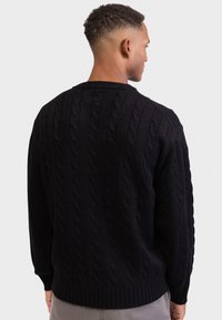 Czarny sweter z dzianiny w splot warkoczowy, z okrągłym dekoltem, długimi rękawami oraz ściągaczami przy mankietach i dole. Tekstura jest gruba i ciepła.