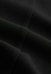 Sort stof med ribbet struktur, der viser vævede detaljer og linjer. Materialet er glat med en let glans, foldet for at afsløre lag.