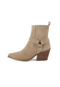 Beige suede ankle boot with a pointed toe, decorative stitching, and a leather strap with metal accents. Slightly raised wooden heel.
