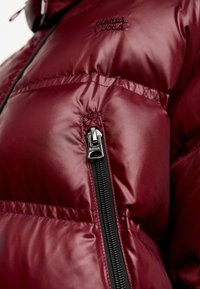 Bordowa kurtka puchowa z błyszczącą, pikowaną fakturą i czarnym zamkiem błyskawicznym. Na piersi i kieszeni bocznej na zamek znajduje się haftowane logo.